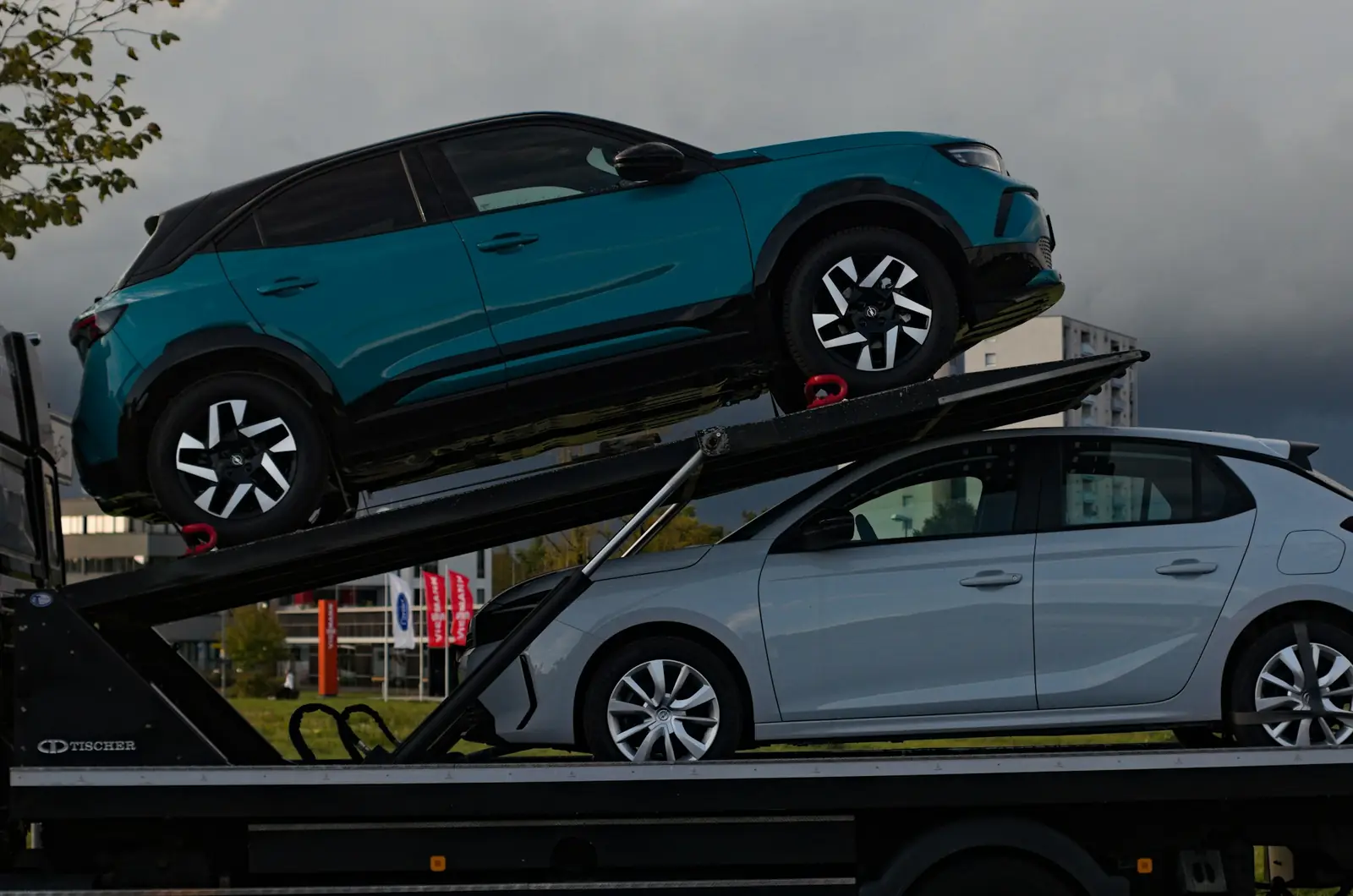 Two cars strapped onto a car carrier under a stormy sky